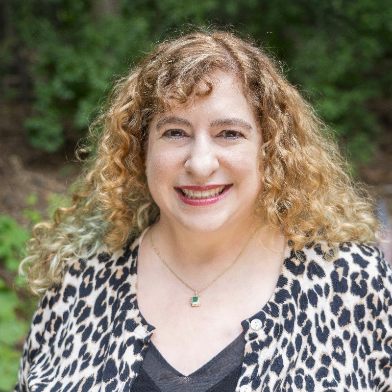 Photo of Lisa Sherwin Wulf. Woman with long curly light brown/blonde hair wearing an animal print cardigan